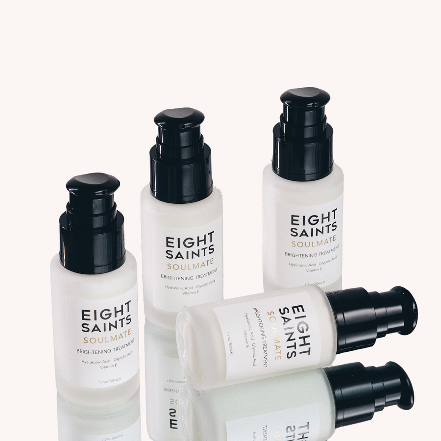 Four bottles of Eight Saints Soulmate Brightening Treatment with Hyaluronic Acid and Vitamin E on a reflective surface