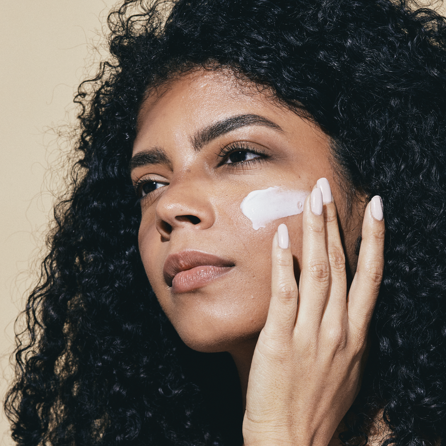 Woman with curly hair applying facial cream.